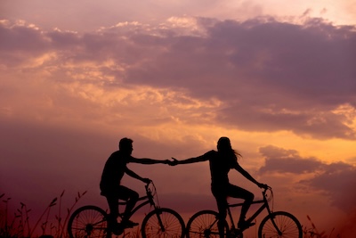 Silhouette of two cyclists reaching for each other at sunset, representing the connection between businesses and customers through virtual phone numbers