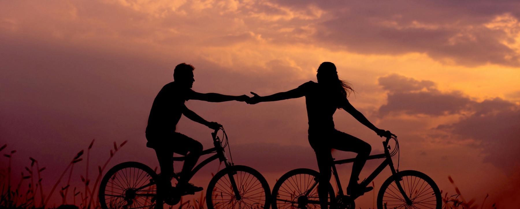 Silhouette of two cyclists reaching for each other at sunset, representing the connection between businesses and customers through virtual phone numbers