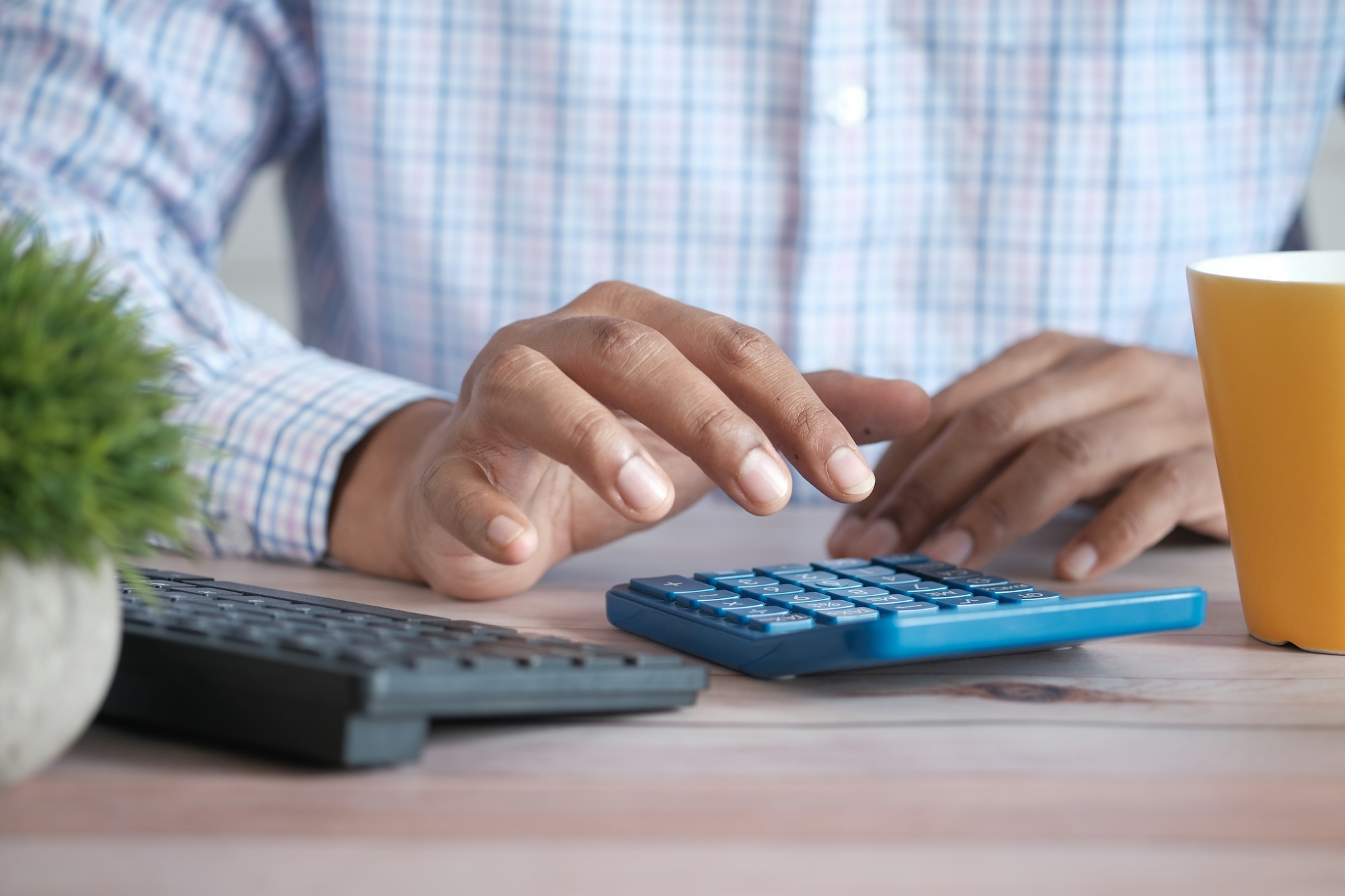 Person using a calculator at a desk, representing accountants managing client finances from a home office