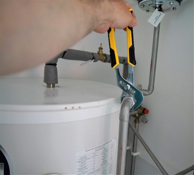 Plumber using pliers to tighten a pipe on a boiler, representing the UK plumbing industry