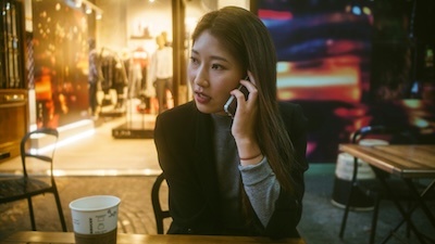 Woman talking on a mobile phone at a cafe in the evening, representing professional business call handling on the go