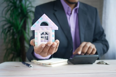 Property manager in a suit holding a small house model and using a calculator, representing property management professionals