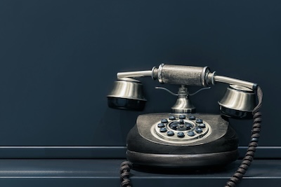 Silver vintage rotary telephone against a dark teal wall, representing traditional business landlines being replaced